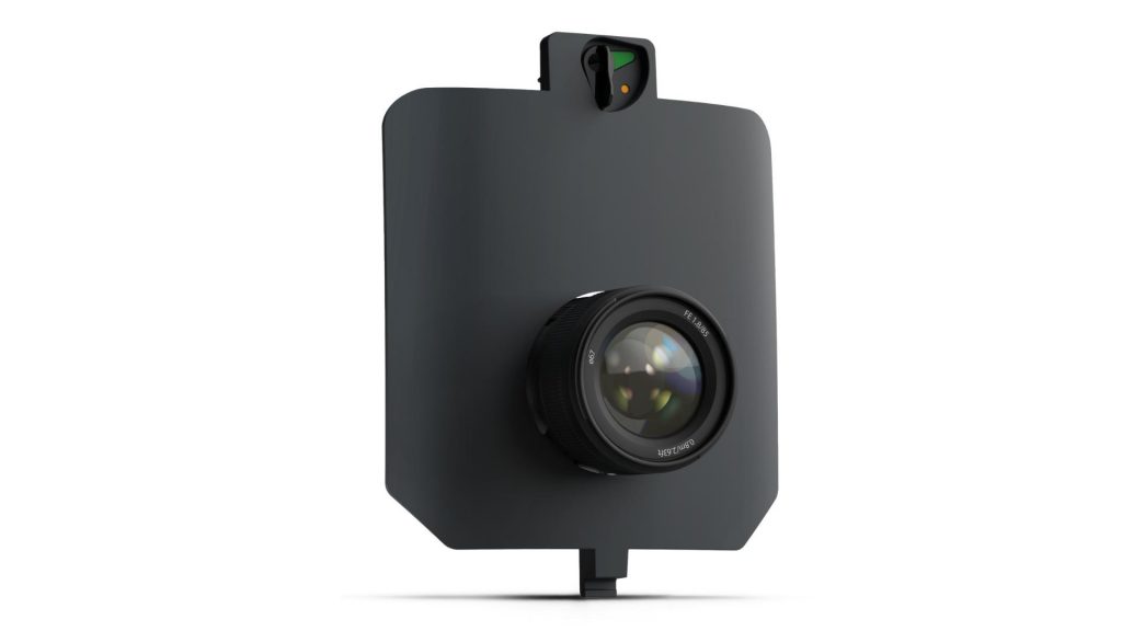 L'Aile Volante WingtraRAY présente un grand objectif de caméra noir monté sur un panneau noir plat et rectangulaire avec une petite protubérance supérieure et une extension inférieure étroite, semblable aux modèles utilisés sur les drones WingtraOne. L'arrière-plan est blanc.