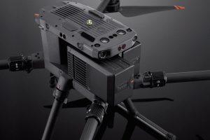 Gros plan sur la batterie de vol intelligente DJI TB65, qui se caractérise par un design noir robuste avec des interfaces de commande et des voyants lumineux bien visibles, posée sur une surface noire réfléchissante.
