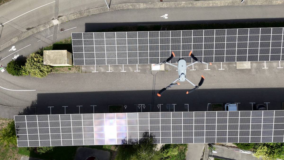 Un drone survole deux parkings couverts dont les toits sont équipés de panneaux solaires, vus d'une vue aérienne lors d'une journée ensoleillée.