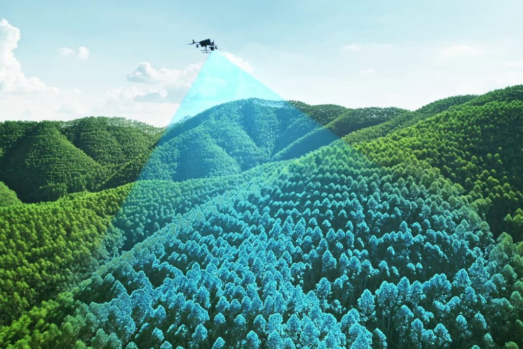Un drone DJI L3 LiDAR plane au-dessus d'une forêt luxuriante, projetant un faisceau de balayage bleu sur les arbres pour cartographier le paysage, avec des collines et un ciel généralement dégagé en arrière-plan.