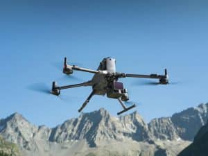 Un drone quadcopter DJI L3 LiDAR équipé d'une caméra vole devant des montagnes escarpées et ensoleillées sous un ciel bleu clair.