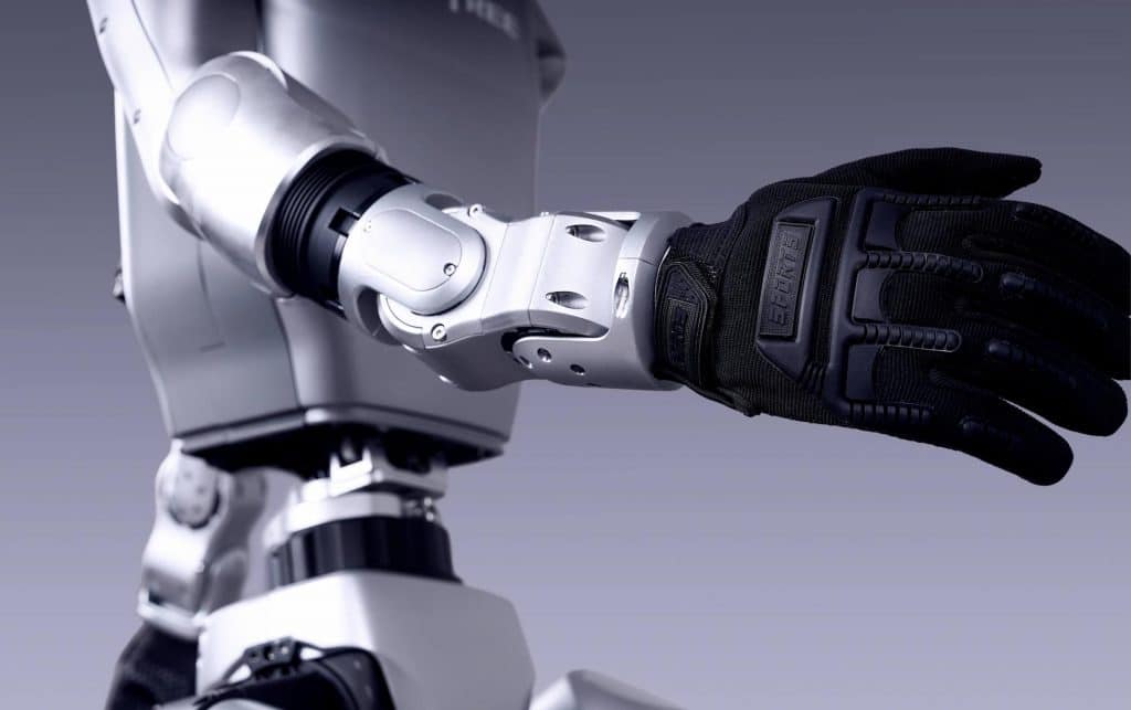 Gros plan sur le bras d'un robot humanoïde Unitree G1 portant un gant noir rembourré, mettant en évidence ses articulations métalliques détaillées et sa surface grise lisse, sur fond de dégradé doux.