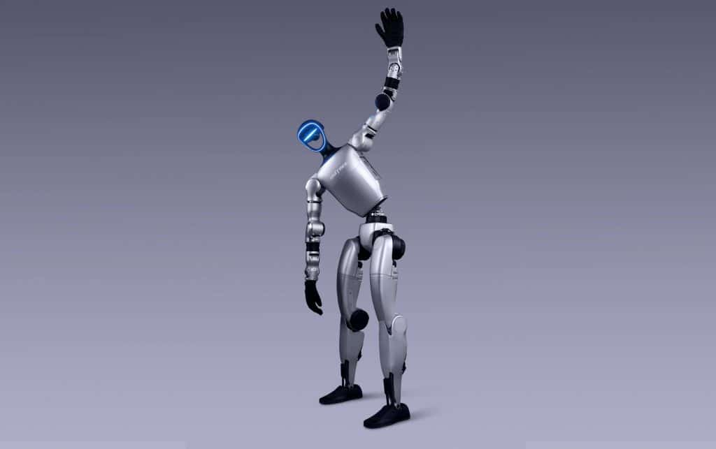 Un robot humanoïde argenté, ressemblant à l'Unitree G1 avec des articulations noires, se tient debout sur une jambe, levant son bras droit tandis que son bras gauche pend, comme s'il s'étirait ou s'agitait. L'arrière-plan est un dégradé gris clair uni.