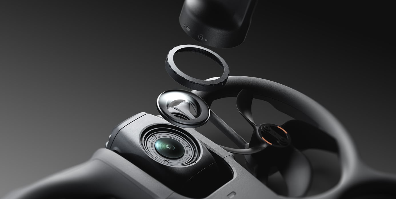 Vue rapprochée d'un objectif de caméra en cours d'assemblage sur le stabilisateur portable moderne et noir DJI Avata 360, avec plusieurs composants d'objectif flottant au-dessus de l'appareil sur un arrière-plan sombre.
