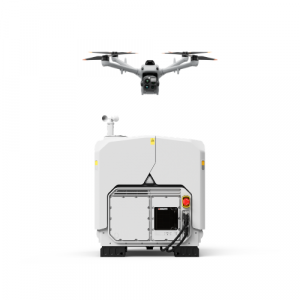 Un drone blanc en vol stationnaire au-dessus d'une station de recharge DJI Dock blanche, de forme cubique.