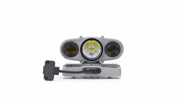 Un module d'éclairage DJI Dock 4 de couleur grise, doté de trois lentilles circulaires et d'un câble d'alimentation intégré.