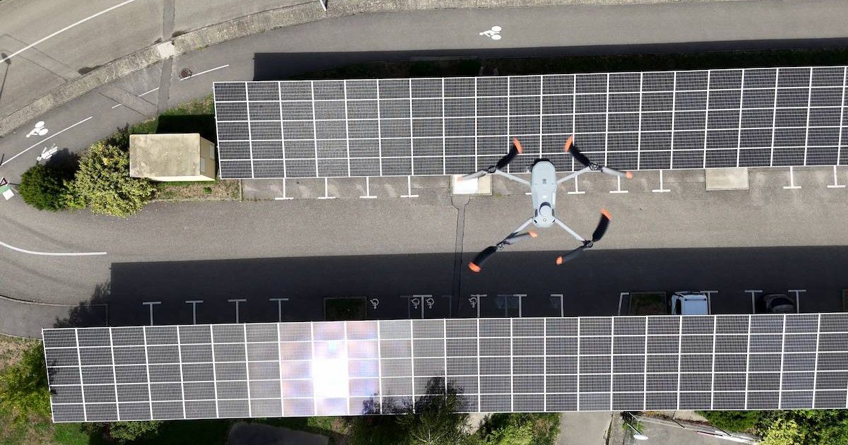 Un drone survole deux parkings couverts dont les toits sont équipés de panneaux solaires, vus d'une vue aérienne lors d'une journée ensoleillée.